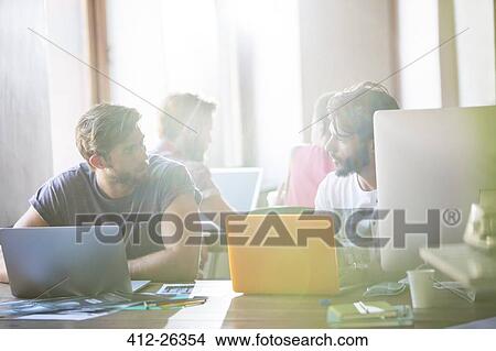 Creative businessmen working at laptops and talking in office View Large Photo Image Picture - Creative businessmen working at laptops and talking in office. Fotosearch