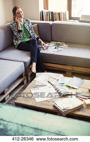Stock Photograph - Creative businesswoman reviewing proofs and talking on cell phone on office sofa. Fotosearch