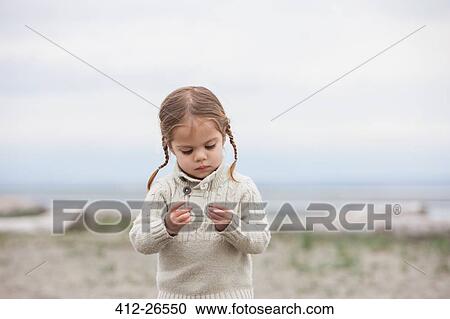 Stock Image - Curious girl examining pebbles on beach. Fotosearch
