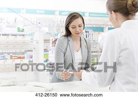 Stock Image - Customer giving prescription to pharmacist in pharmacy. Fotosearch