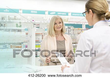 Stock Image - Customer giving prescription to pharmacist in pharmacy. Fotosearch