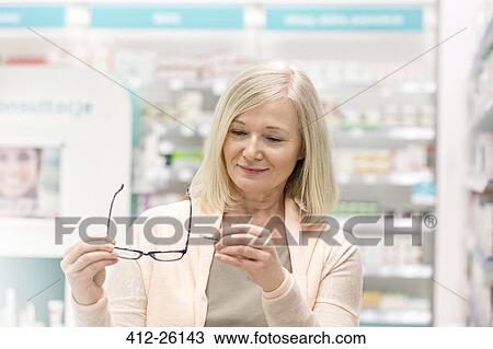 Stock Image - Customer looking at price tag on reading glasses in pharmacy. Fotosearch