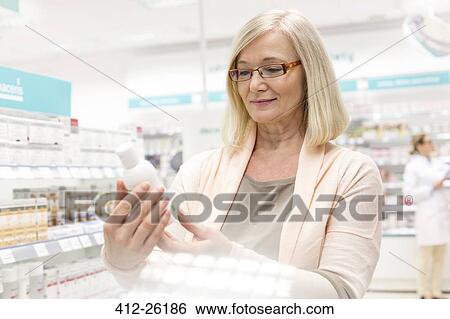 Stock Photograph - Customer reading label on bottle in pharmacy. Fotosearch