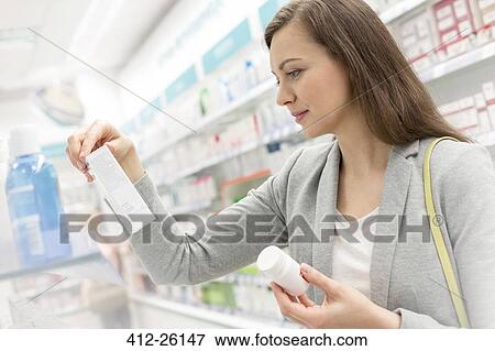 Stock Photo - Customer reading label on box in pharmacy. Fotosearch