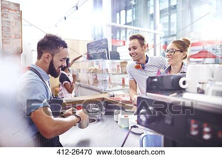 Stock Image - Customers watching barista make coffee in cafe. Fotosearch