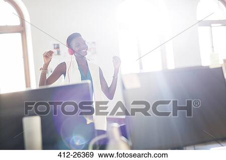 Enthusiastic businesswoman wearing headphones and dancing in office View Large Photo Image Stock Photo - Enthusiastic businesswoman wearing headphones and dancing in office. Fotosearch