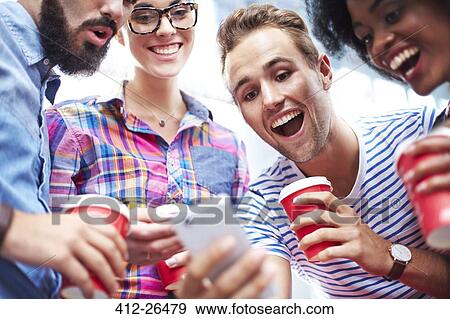 Friends laughing and drinking coffee around cell phone View Large Photo Image Stock Photo - Friends laughing and drinking coffee around cell phone. Fotosearch