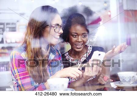 Stock Image - Friends texting at cafe window. Fotosearch