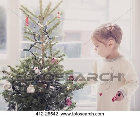 Stock Image - Girl decorating small Christmas tree. Fotosearch