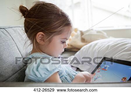 Stock Photo - Girl using digital tablet on sofa. Fotosearch