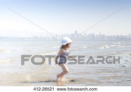 Stock Image - Girl wading in surf on beach. Fotosearch