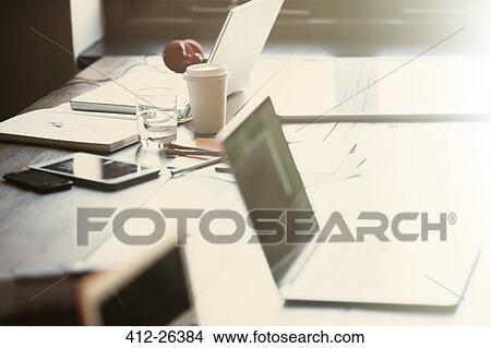 Picture - "Laptops, digital tablet and paperwork on table in sunny office". Fotosearch