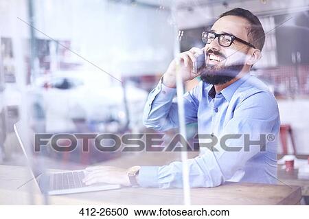 Laughing businessman talking on cell phone at laptop in cafe window View Large Photo Image Stock Image - Laughing businessman talking on cell phone at laptop in cafe window. Fotosearch