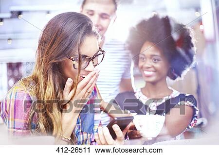 Stock Image - Laughing friends texting with cell phone in cafe. Fotosearch