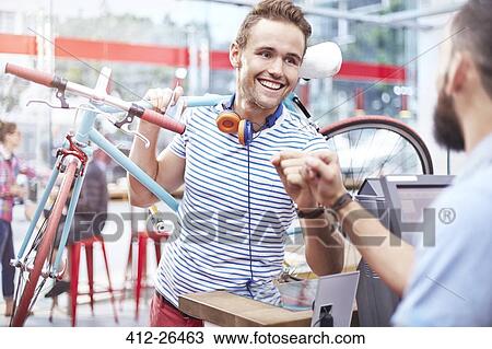 Stock Image - Man with bicycle fist bumping worker in cafe. Fotosearch