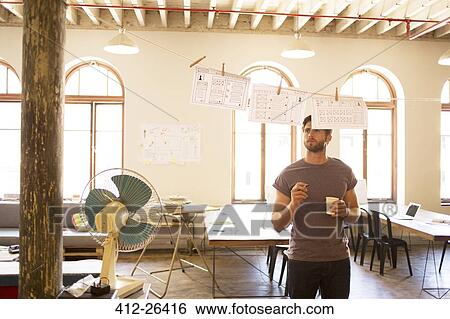 Pensive causal businessman reviewing hanging diagrams in open office View Large Photo Image Stock Photograph - Pensive causal businessman reviewing hanging diagrams in open office. Fotosearch