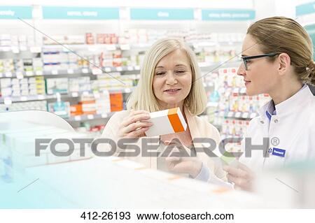 Stock Image - Pharmacist and customer reading label on box in pharmacy. Fotosearch