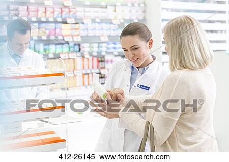 Stock Photography - Pharmacist and customer reviewing label on box in pharmacy. Fotosearch