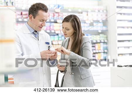 Stock Photo - Pharmacist and customer reviewing prescription label in pharmacy. Fotosearch