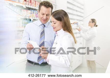 Stock Photo - Pharmacist and customer reviewing prescription in pharmacy. Fotosearch