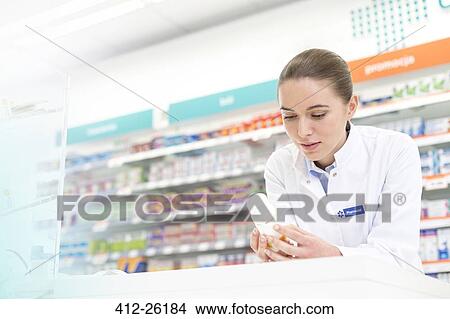 Picture - Pharmacist reading label on bottle in pharmacy. Fotosearch
