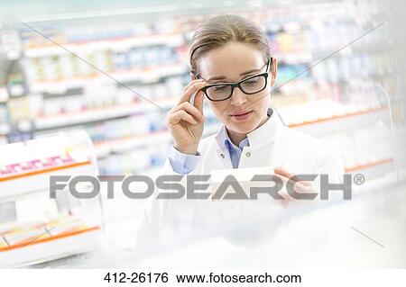 Stock Photograph - Pharmacist reading label on box in pharmacy. Fotosearch