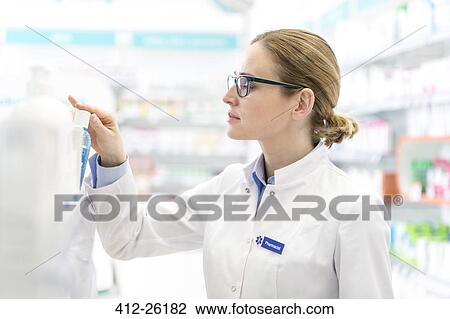 Stock Image - Pharmacist removing bottle from shelf in pharmacy. Fotosearch