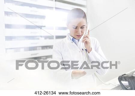 Pharmacist verifying prescription on telephone in pharmacy View Large Photo Image Picture - Pharmacist verifying prescription on telephone in pharmacy. Fotosearch