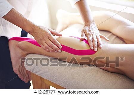 Stock Photo - Physical therapist applying kinesiology tape to man’s leg. Fotosearch