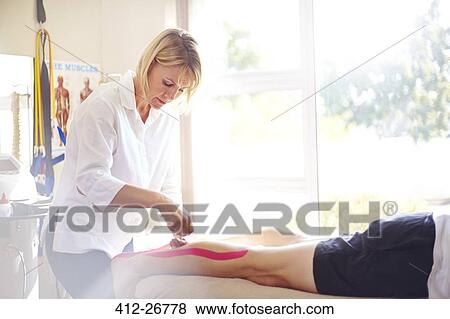 Stock Photo - Physical therapist applying kinesiology tape to man’s leg. Fotosearch