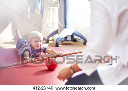 Physical therapist guiding boy rolling ball with stick View Large Photo Image Stock Photograph - Physical therapist guiding boy rolling ball with stick. Fotosearch