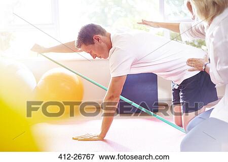Stock Photo - Physical therapist guiding man pulling resistance band. Fotosearch
