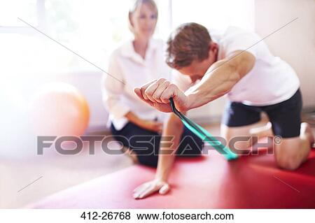 Stock Photo - Physical therapist guiding man pulling resistance band. Fotosearch