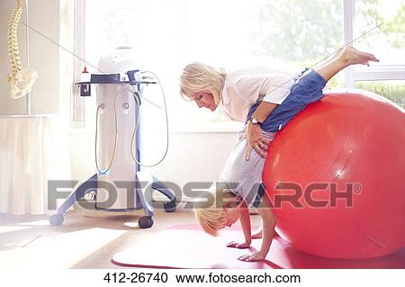 Physical therapist holding boy over large fitness ball View Large Photo Image Stock Image - Physical therapist holding boy over large fitness ball. Fotosearch