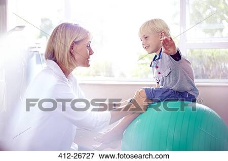 Physical therapist holding boy with arms outstretched on fitness ball View Large Photo Image Stock Photo - Physical therapist holding boy with arms outstretched on fitness ball. Fotosearch