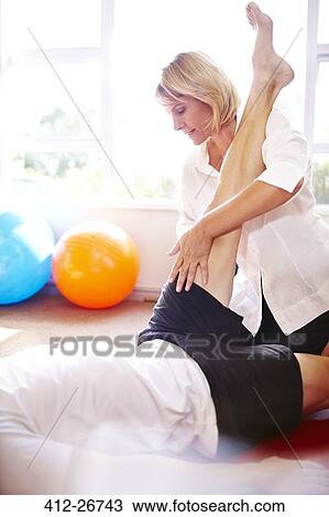 Stock Image - Physical therapist stretching man’s leg. Fotosearch