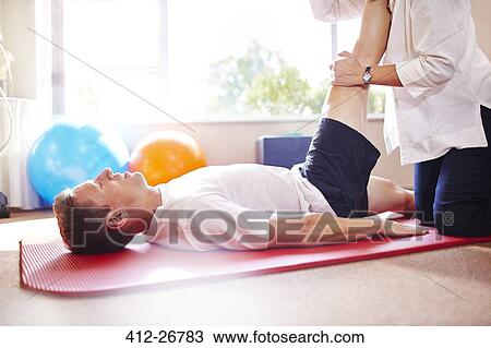 Stock Image - Physical therapist stretching man’s leg. Fotosearch