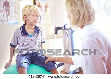Stock Image - Physical therapist talking to boy on fitness ball. Fotosearch