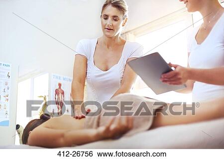Stock Photograph - Physical therapists with digital tablet massaging woman’s back. Fotosearch