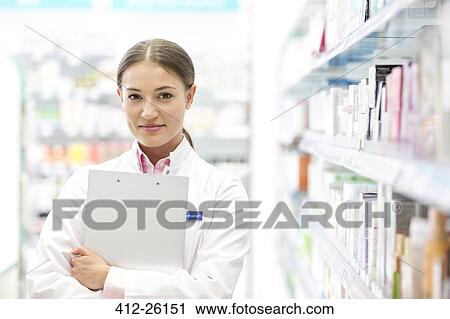 Stock Image - Portrait of confident pharmacist holding clipboard in pharmacy. Fotosearch