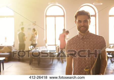 Stock Photo - Portrait smiling casual businessman with skateboard in sunny open office. Fotosearch