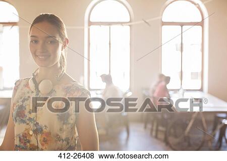 Stock Photo - Portrait smiling casual businesswoman with headphones in sunny open office. Fotosearch