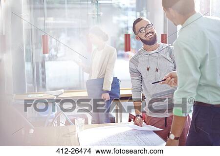 Picture - Smiling architects talking and reviewing blueprints. Fotosearch