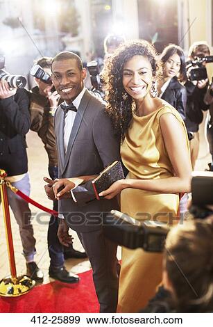 Smiling celebrity couple being photographed by paparazzi photographers at red carpet event View Large Photo Image Stock Photo - Smiling celebrity couple being photographed by paparazzi photographers at red carpet event. Fotosearch
