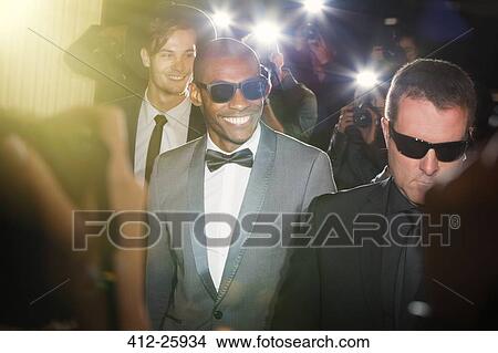 Picture - Smiling celebrity in sunglasses being photographed by paparazzi photographers at event. Fotosearch
