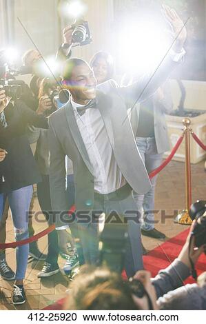 Stock Image - Smiling celebrity waving and being photographed by paparazzi photographers. Fotosearch