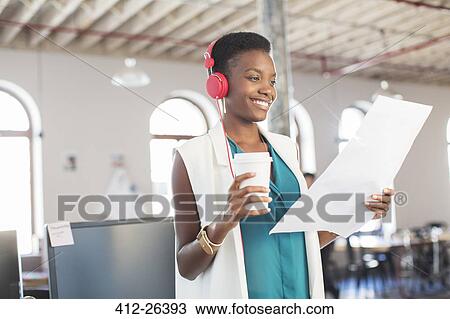 Smiling creative businesswoman with headphones and coffee reviewing paperwork in office View Large Photo Image Stock Image - Smiling creative businesswoman with headphones and coffee reviewing paperwork in office. Fotosearch