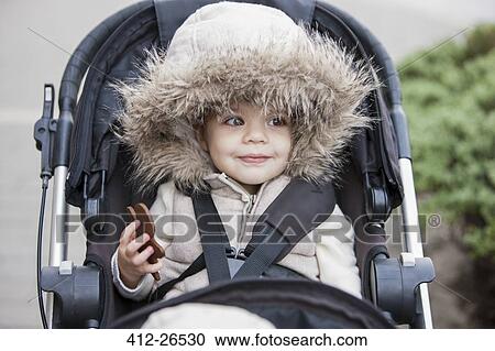 Stock Image - Smiling girl in fur hood riding in stroller. Fotosearch