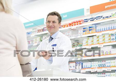 Stock Image - Smiling pharmacist assisting customer in pharmacy. Fotosearch