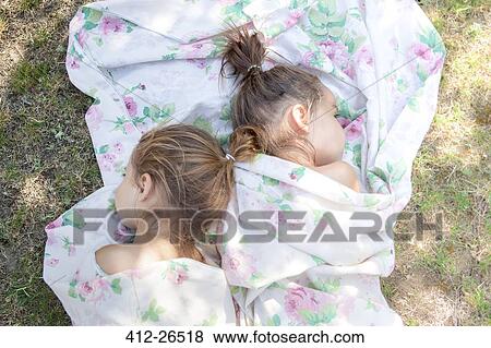 Stock Photo - Twin girls napping in floral sheet on grass. Fotosearch
